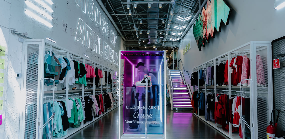 Imagem interna da loja da Authentic Feet. Loja possui cores brancas, cabines de roupas no meio e com tênis à direita, e prateleira à esquerda com chapéus