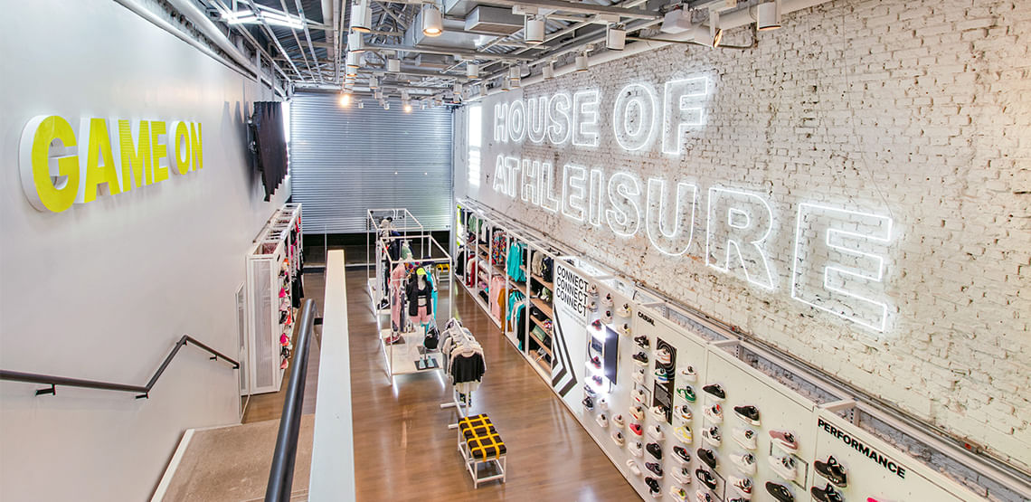 Imagem interna da loja da Authentic Feet. Loja possui cores brancas, cabines de roupas no meio e com tênis à direita, e prateleira à esquerda com chapéus
